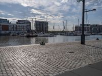 the pavement has stone pavers on it and boats are parked outside in the harbor