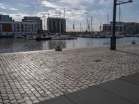 the pavement has stone pavers on it and boats are parked outside in the harbor