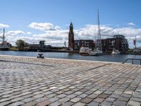 a brick sidewalk is lined up along with boats and buildings in the background on a sunny day