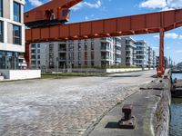 a brick street next to a bridge spanning with buildings along the side of a body of water