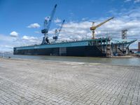 a large ship with crane on deck next to it in the water near docks and cranes