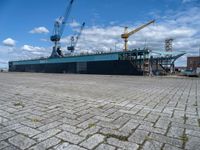 a large ship with crane on deck next to it in the water near docks and cranes