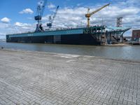 a large ship with crane on deck next to it in the water near docks and cranes