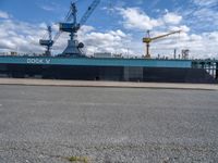 the large blue ship is parked near a dock and a large crane in the background