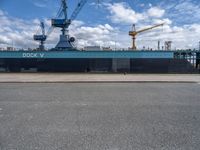 the large blue ship is parked near a dock and a large crane in the background