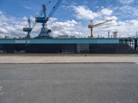 the large blue ship is parked near a dock and a large crane in the background