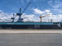 the large blue ship is parked near a dock and a large crane in the background