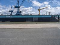 the large blue ship is parked near a dock and a large crane in the background