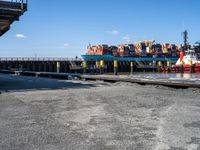 a long dock filled with lots of cargo boats and docked ships by the water or on a calm day