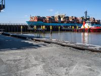 a long dock filled with lots of cargo boats and docked ships by the water or on a calm day