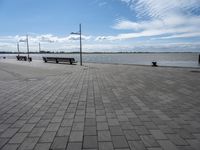 the pavement is paved with stones near the water and a bench on top of it