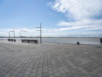 the pavement is paved with stones near the water and a bench on top of it