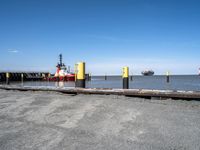 a red and yellow boat floating next to a dock with large tugboats in the water