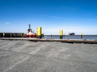 a red and yellow boat floating next to a dock with large tugboats in the water