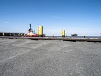 a red and yellow boat floating next to a dock with large tugboats in the water