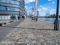 a paved walkway next to the sea with tall buildings on either side and sailboats in distance