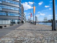 a paved walkway next to the sea with tall buildings on either side and sailboats in distance