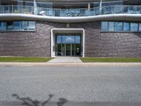 a large building is next to the street that leads up to it, and shows an archway leading through to a staircase, with a long white railing and curved door and grass field on either side walkway