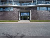 a large building is next to the street that leads up to it, and shows an archway leading through to a staircase, with a long white railing and curved door and grass field on either side walkway