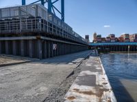 a man on a bike passes an open bridge over water with containers and shipping containers in the background