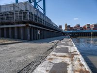 a man on a bike passes an open bridge over water with containers and shipping containers in the background