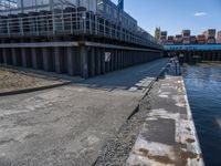 a man on a bike passes an open bridge over water with containers and shipping containers in the background