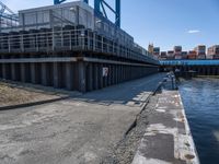 a man on a bike passes an open bridge over water with containers and shipping containers in the background