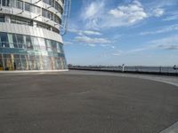 an empty paved concrete area next to water and a tall building in the background with large glass windows