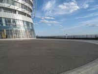 an empty paved concrete area next to water and a tall building in the background with large glass windows