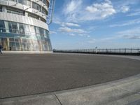 an empty paved concrete area next to water and a tall building in the background with large glass windows