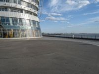 an empty paved concrete area next to water and a tall building in the background with large glass windows