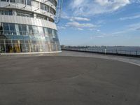 an empty paved concrete area next to water and a tall building in the background with large glass windows