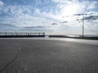 a skateboarder jumps on the pavement in front of a pier in sunny weather