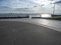 a skateboarder jumps on the pavement in front of a pier in sunny weather