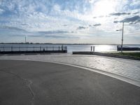 a skateboarder jumps on the pavement in front of a pier in sunny weather