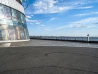 an empty empty street next to a building near the water and a large sky in the background