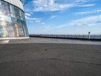 an empty empty street next to a building near the water and a large sky in the background