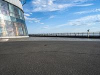 an empty empty street next to a building near the water and a large sky in the background