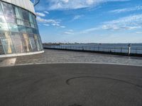 an empty empty street next to a building near the water and a large sky in the background