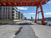 an overpass on a road next to buildings and water in front of them is a train