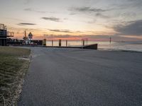 the sun sets on the horizon over a harbor and a boat dock with a man walking in front of it