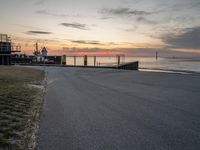 the sun sets on the horizon over a harbor and a boat dock with a man walking in front of it