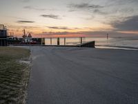 the sun sets on the horizon over a harbor and a boat dock with a man walking in front of it