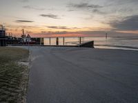 the sun sets on the horizon over a harbor and a boat dock with a man walking in front of it