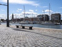 a stone sidewalk next to water and boats in the harbor area of a city,