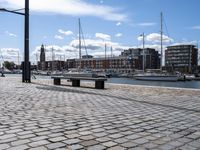 a stone sidewalk next to water and boats in the harbor area of a city,