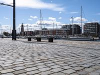 a stone sidewalk next to water and boats in the harbor area of a city,