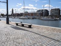 a stone sidewalk next to water and boats in the harbor area of a city,