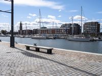 a stone sidewalk next to water and boats in the harbor area of a city,