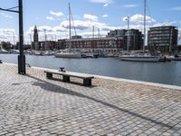 a stone sidewalk next to water and boats in the harbor area of a city,